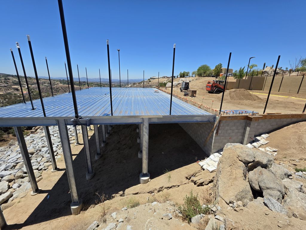 Elevated steel-framed deck on steel columns built into a rocky hillside under clear sky