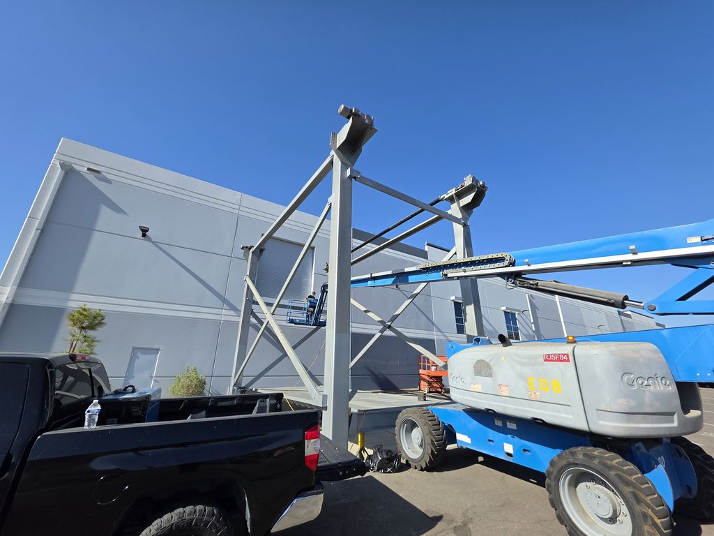 Braced structural steel frame being installed beside a commercial building, with a boom lift in position