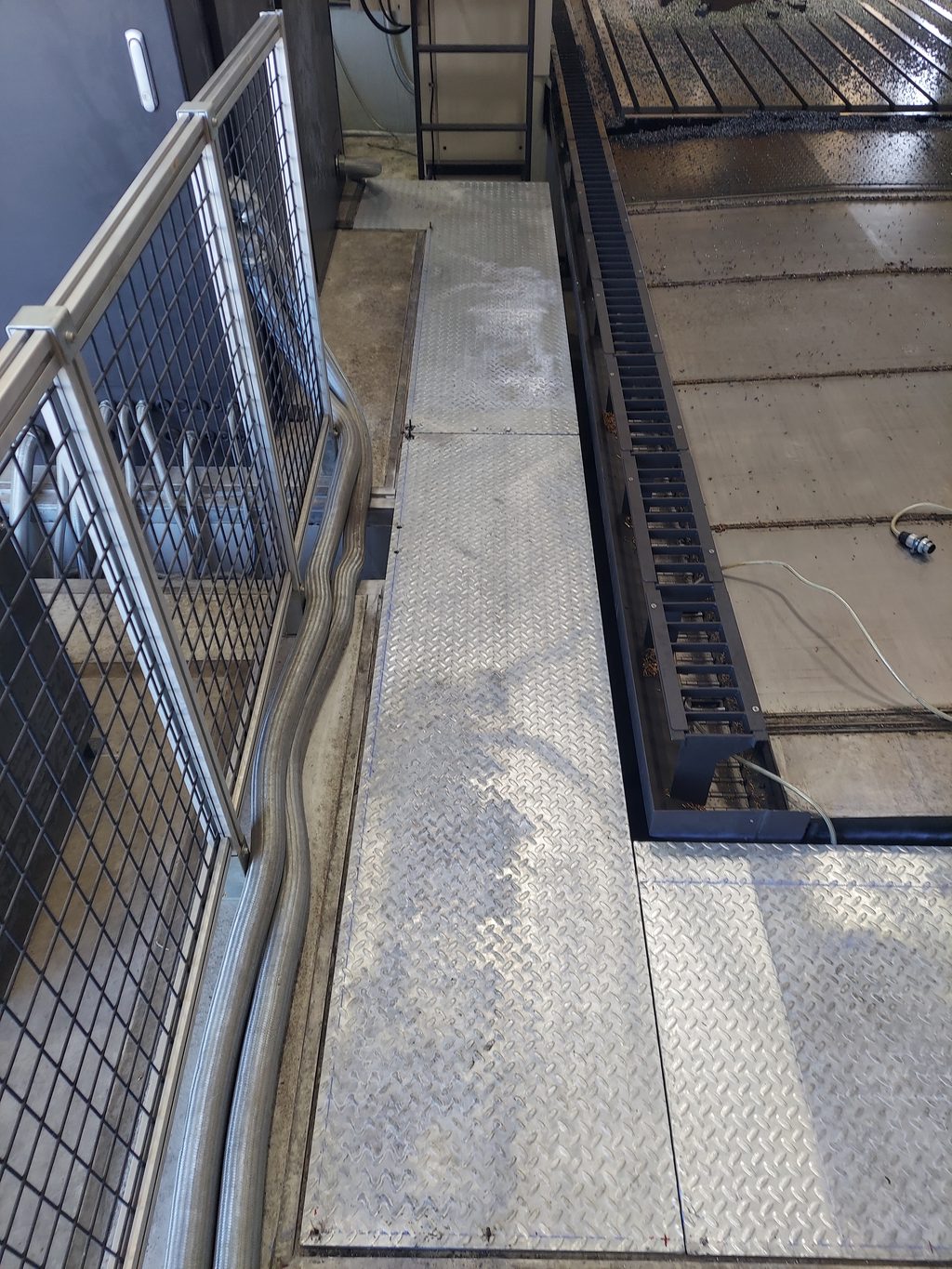 Diamond-plate steel walkway running alongside a large industrial machine, with a welded mesh guard railing on one side